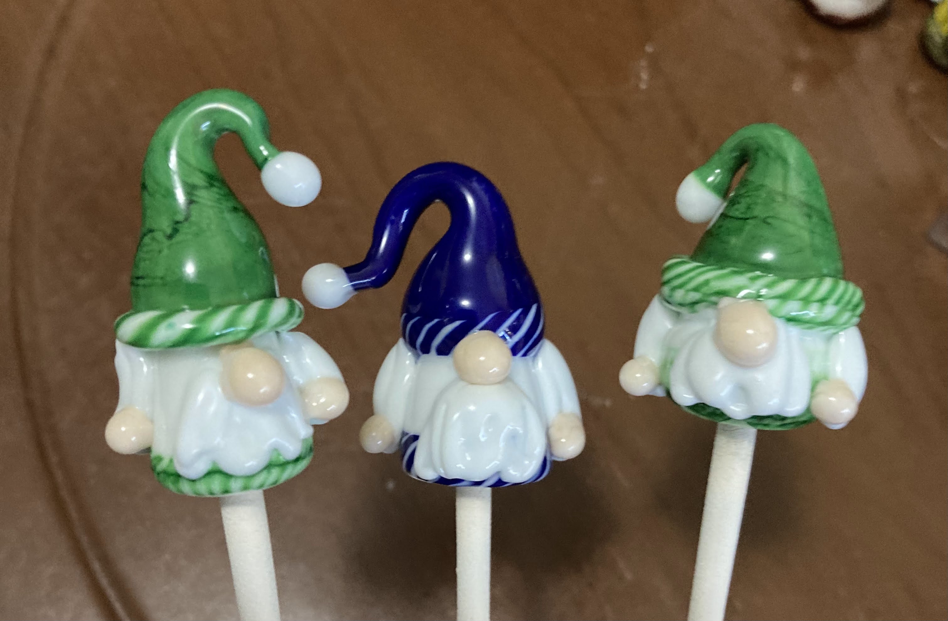 Three colorful handmade glass gnomes with green and blue hats